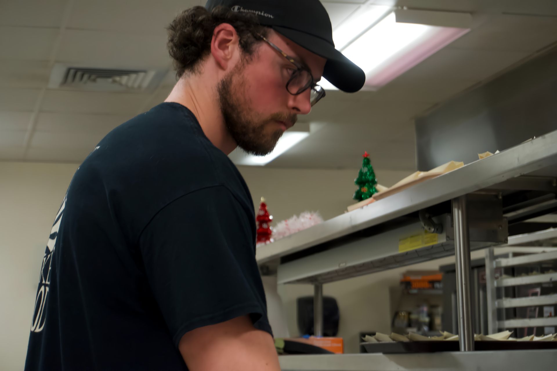 A man wearing a hat and glasses is working in a kitchen.