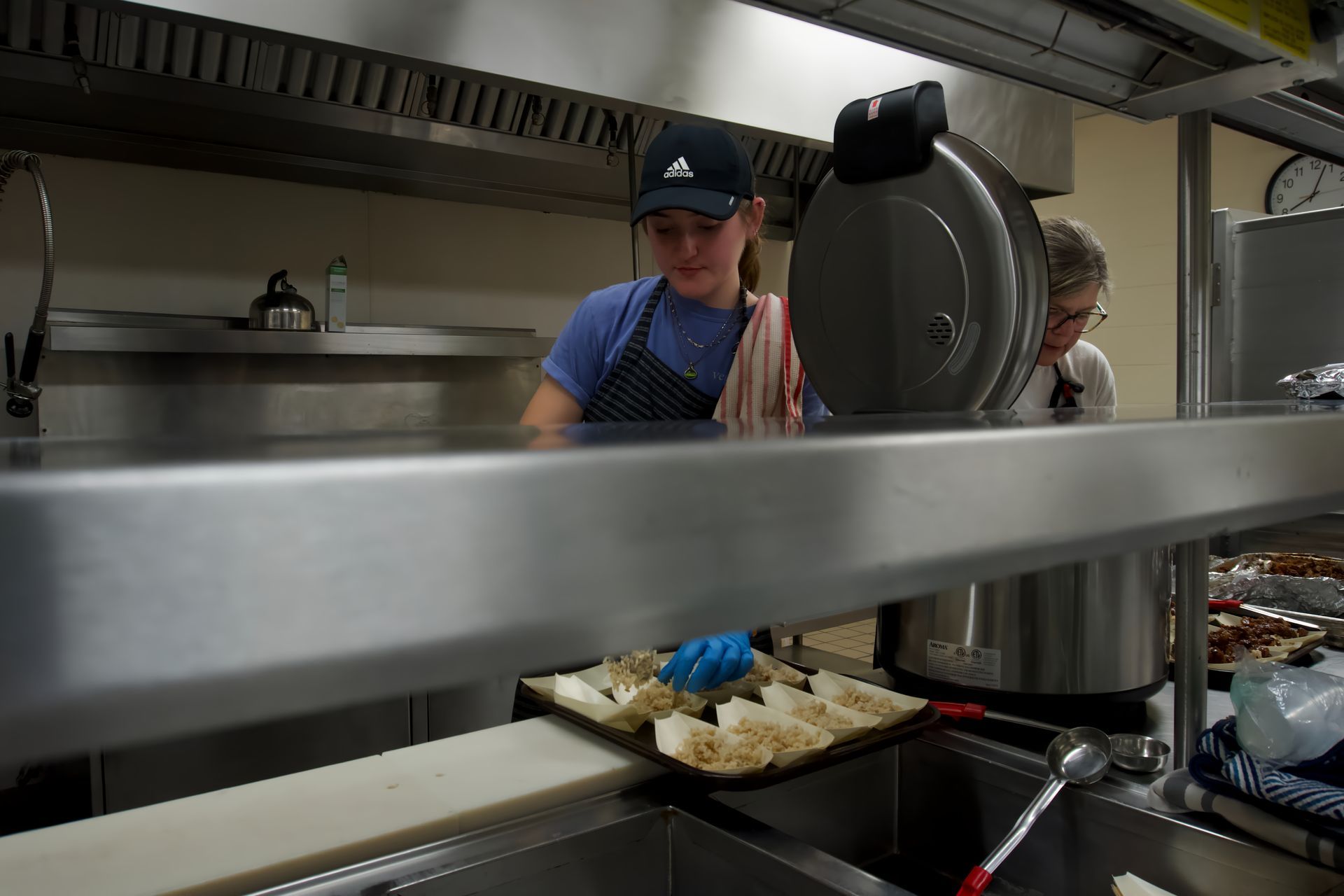 A woman in an adidas hat is cooking in a kitchen