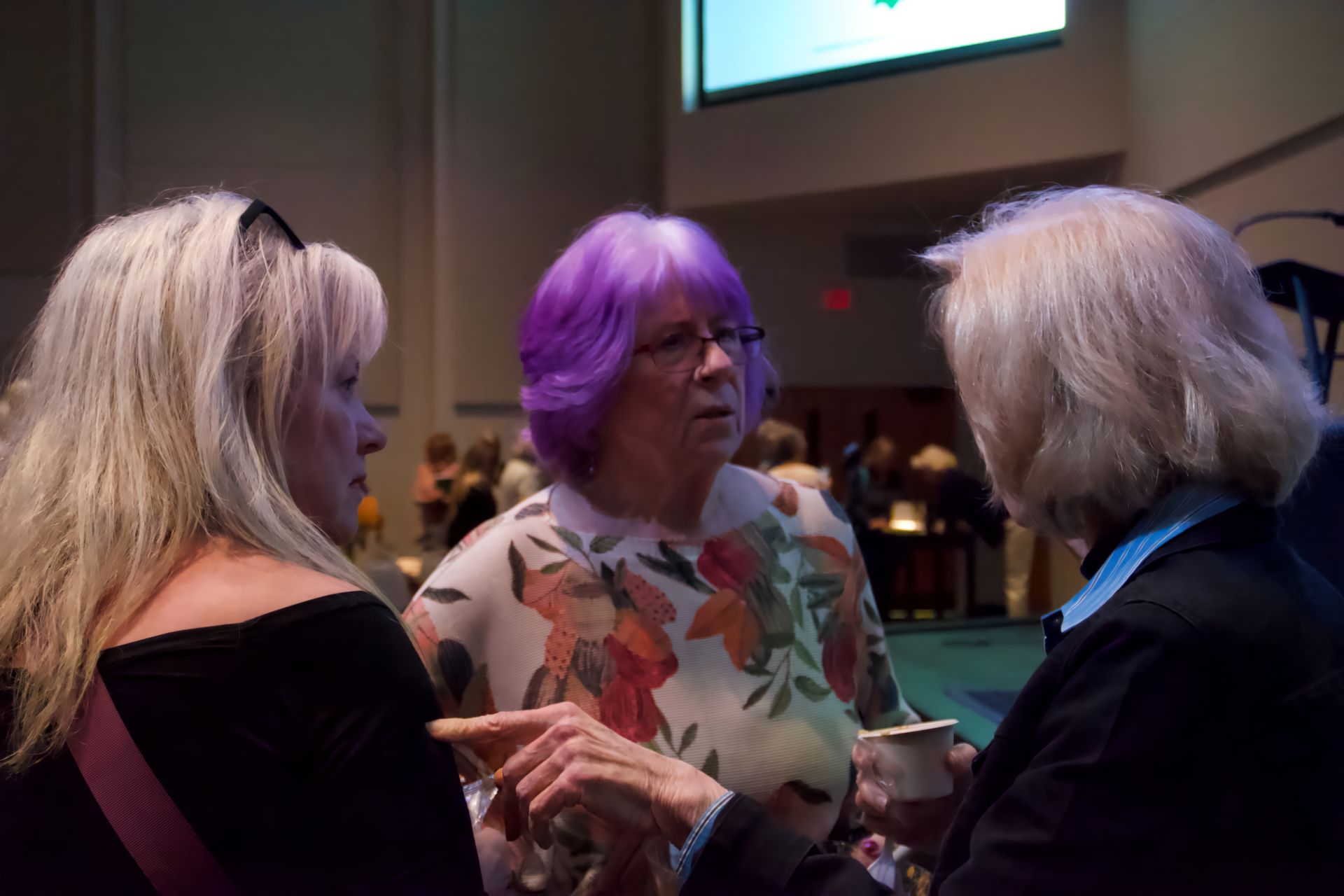 Three women with purple hair are talking to each other in a room.