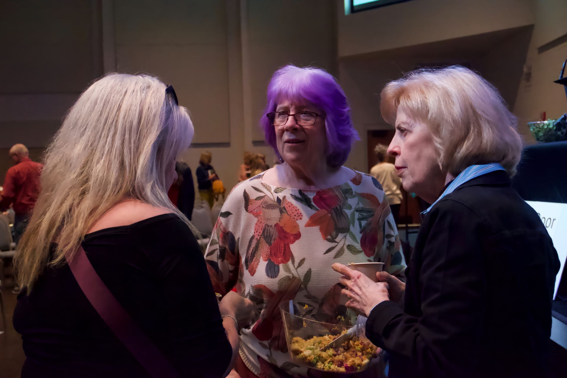 A woman with purple hair is talking to two other women