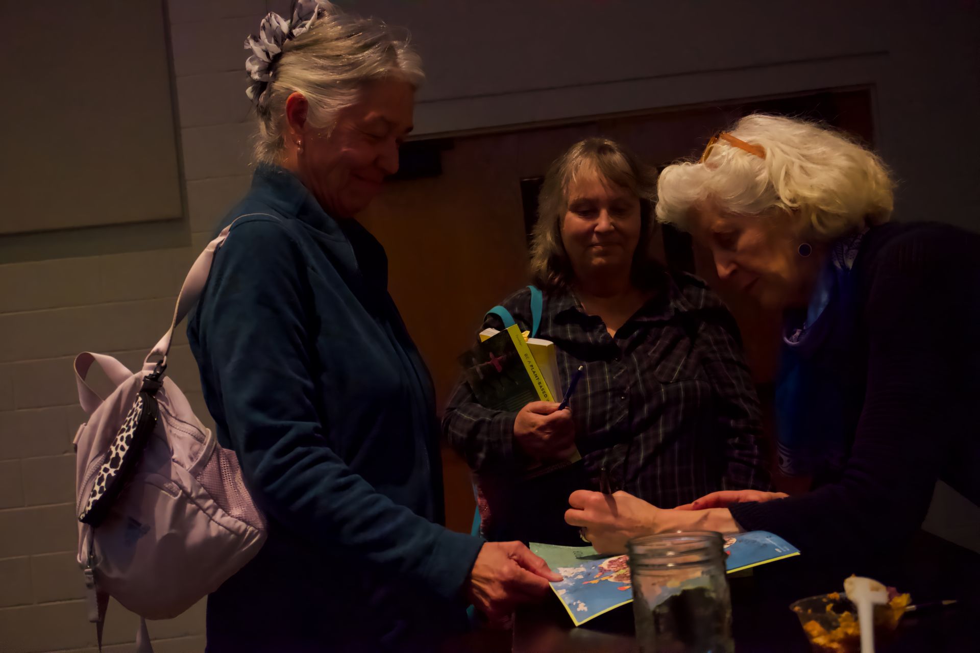 Three women are standing around a table talking to each other.