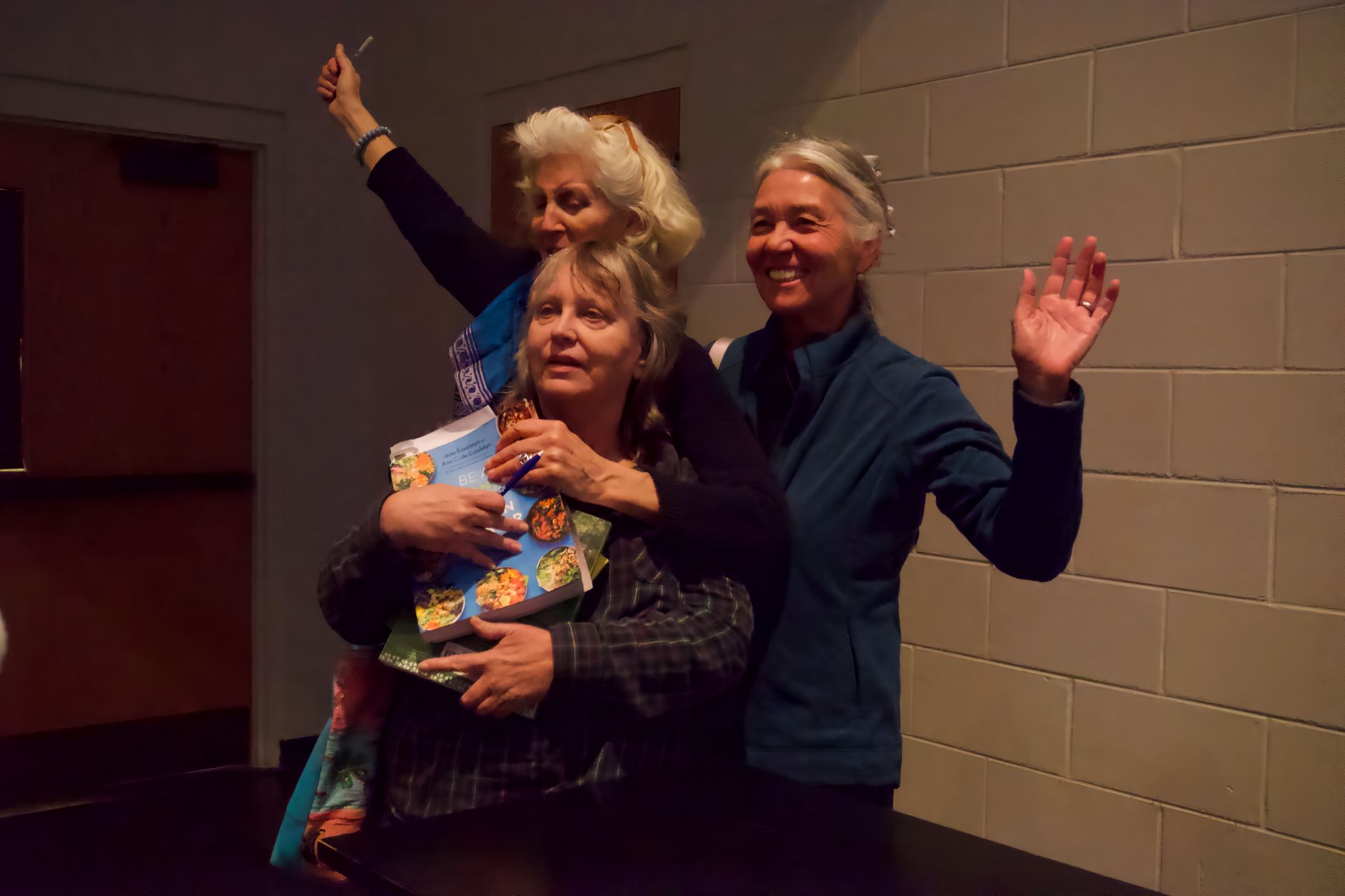 Three women are standing next to each other in front of a brick wall.