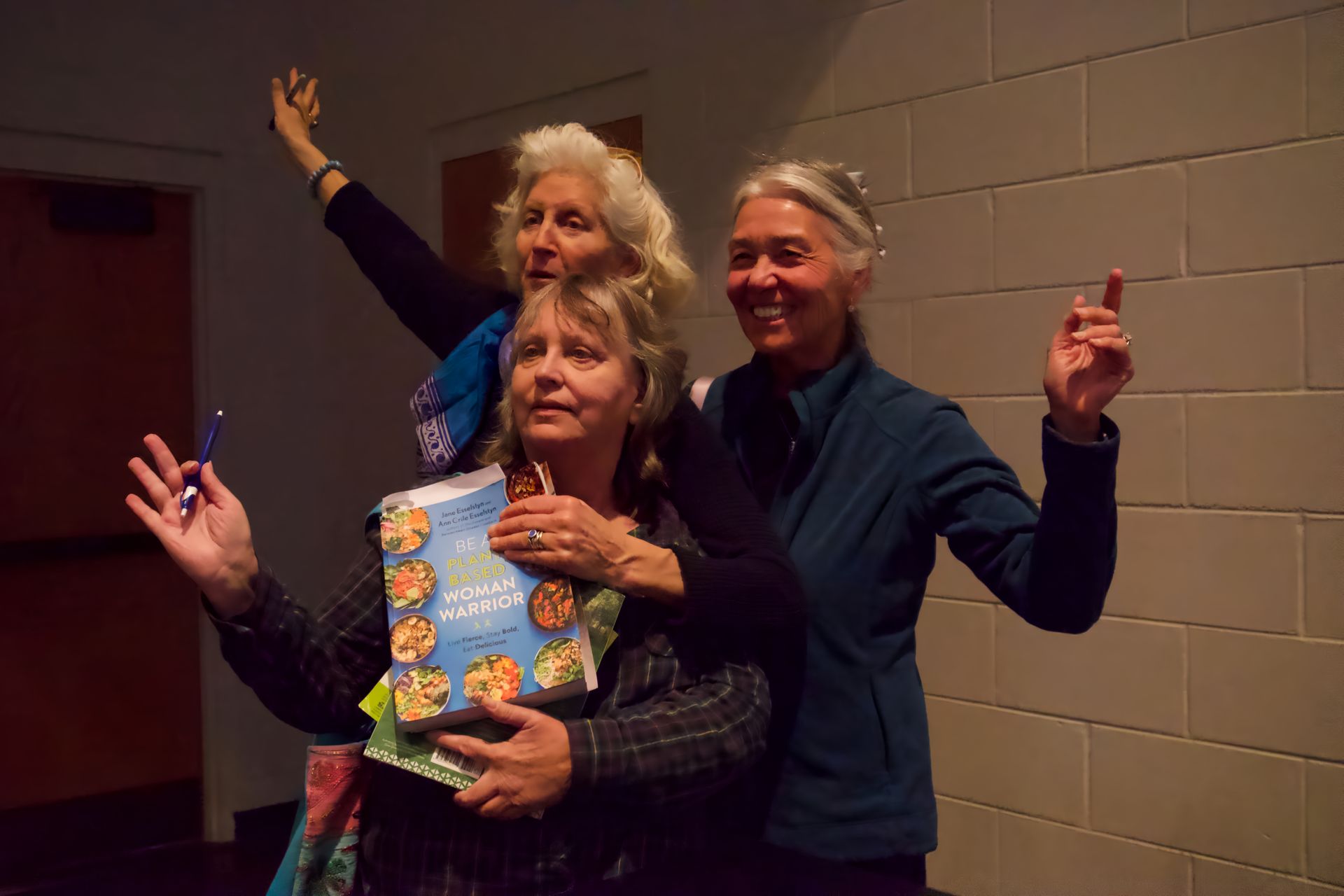 Three older women are posing for a picture in front of a brick wall.
