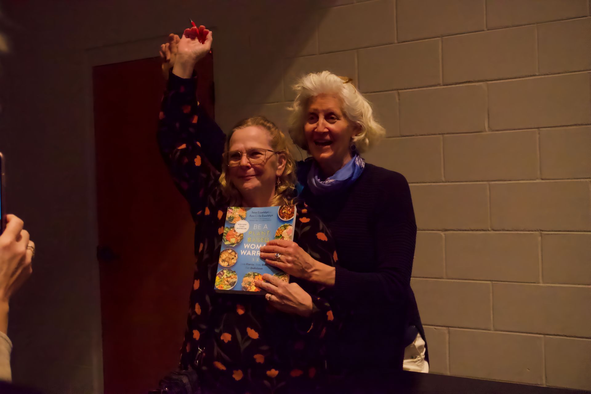 Two women are standing next to each other holding a book in their hands.