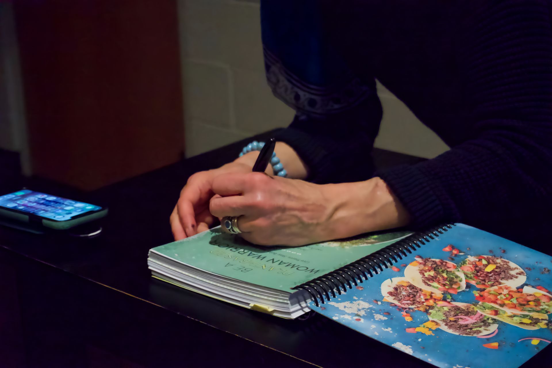 A person is writing in a notebook next to a cell phone