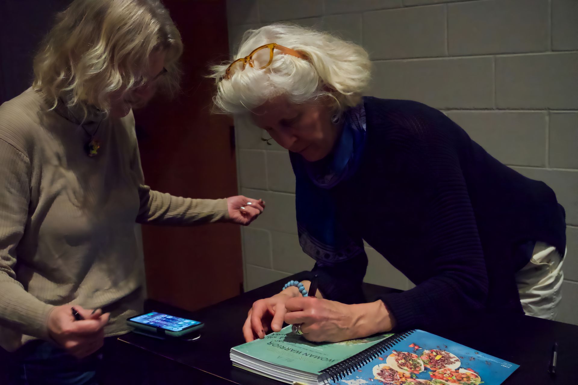 Two women are sitting at a table looking at a book