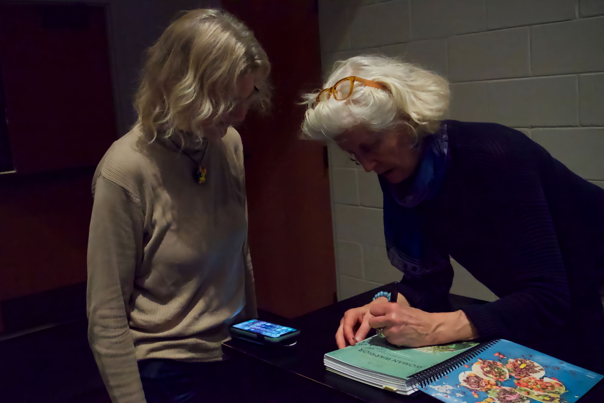 A woman is signing a book while another woman looks on.