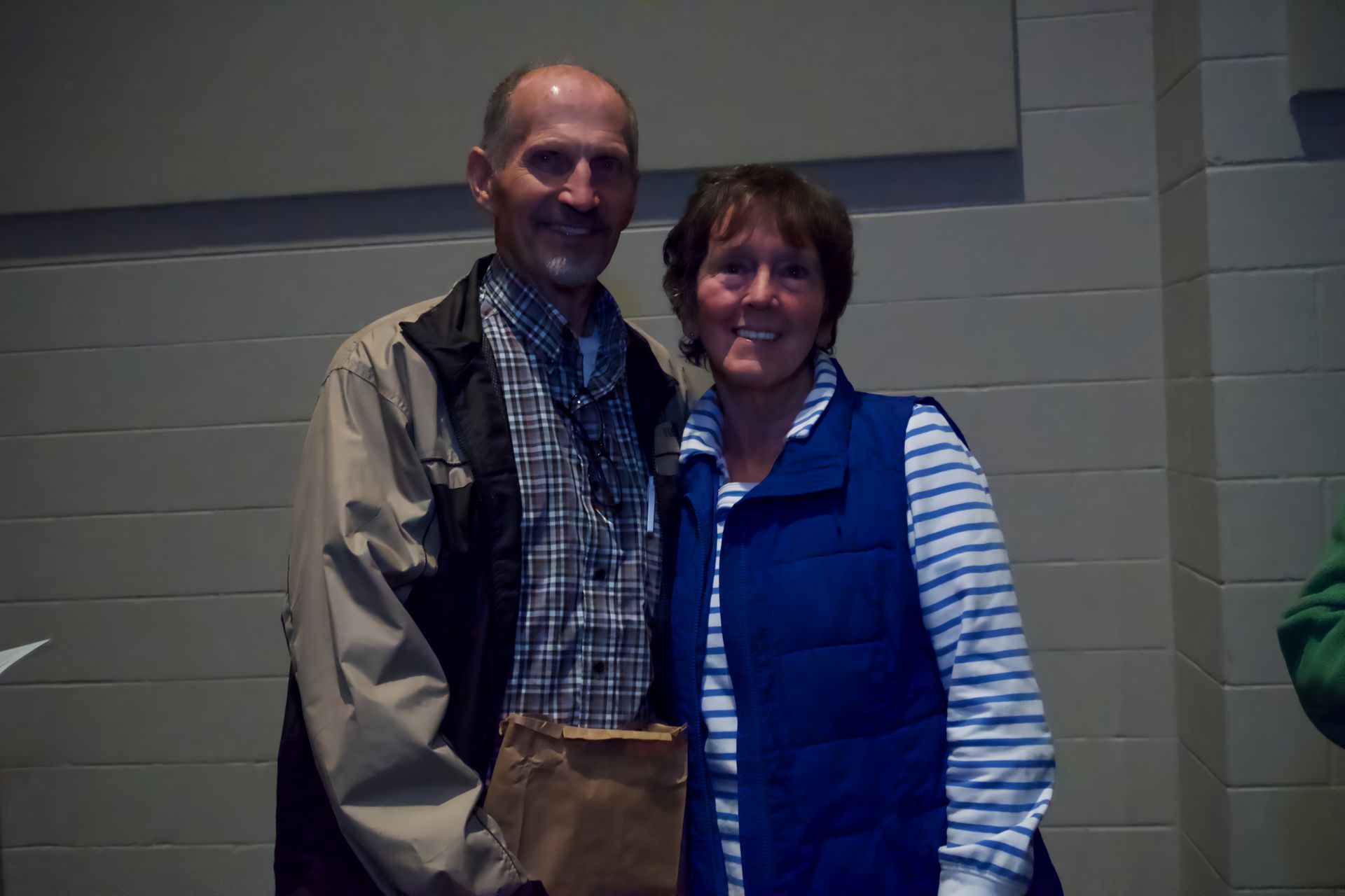 A man and a woman are posing for a picture . the woman is wearing a blue vest.