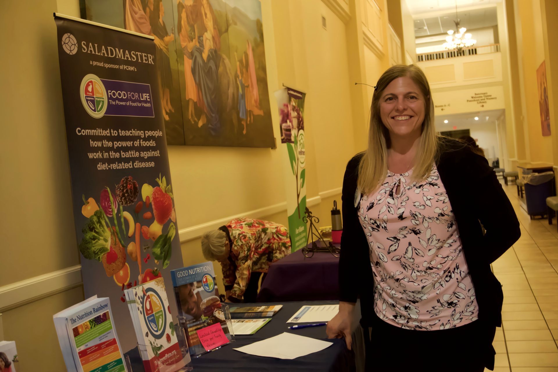A woman is standing in front of a table with a saladmaster sign on it.