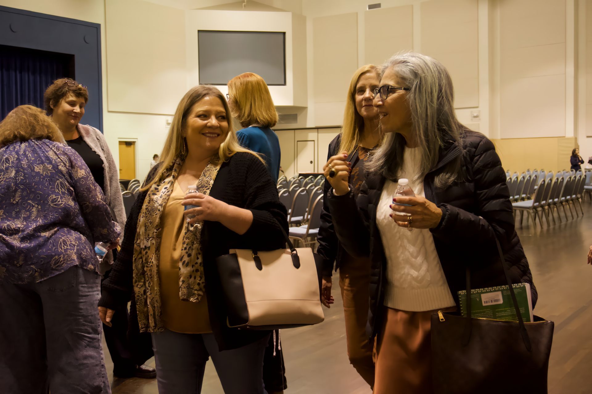 A group of women are standing in a room talking to each other.