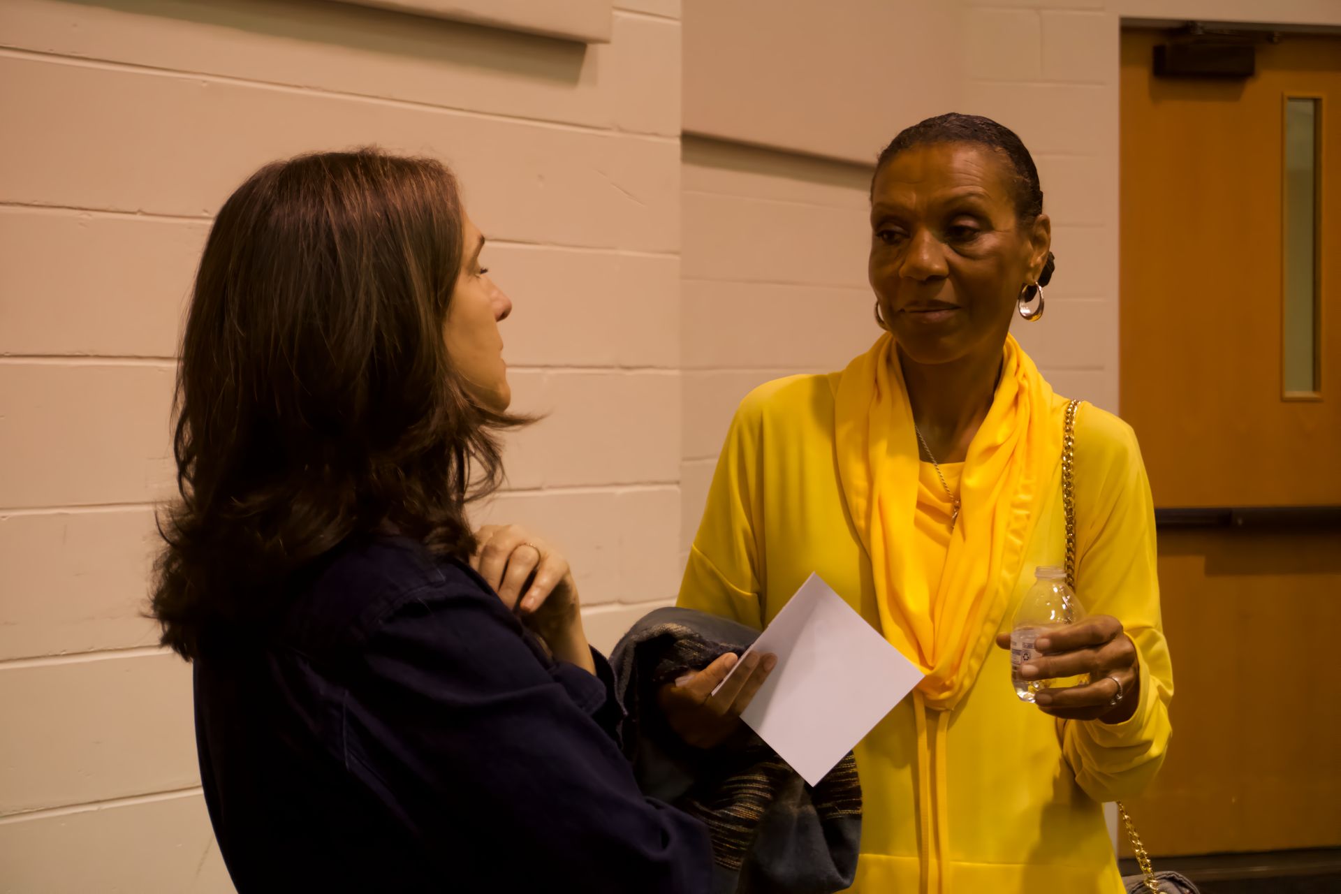 Two women are standing next to each other and talking . one of the women is wearing a yellow scarf.