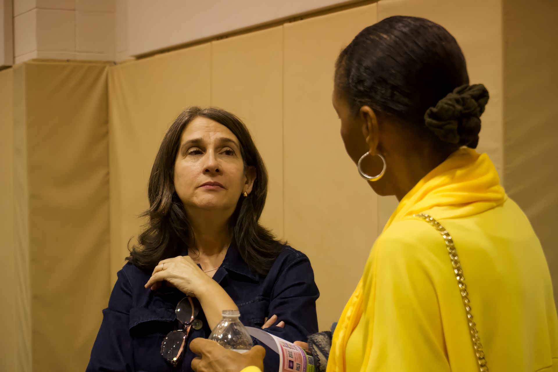 Two women are talking to each other in a room while one woman is holding a water bottle.
