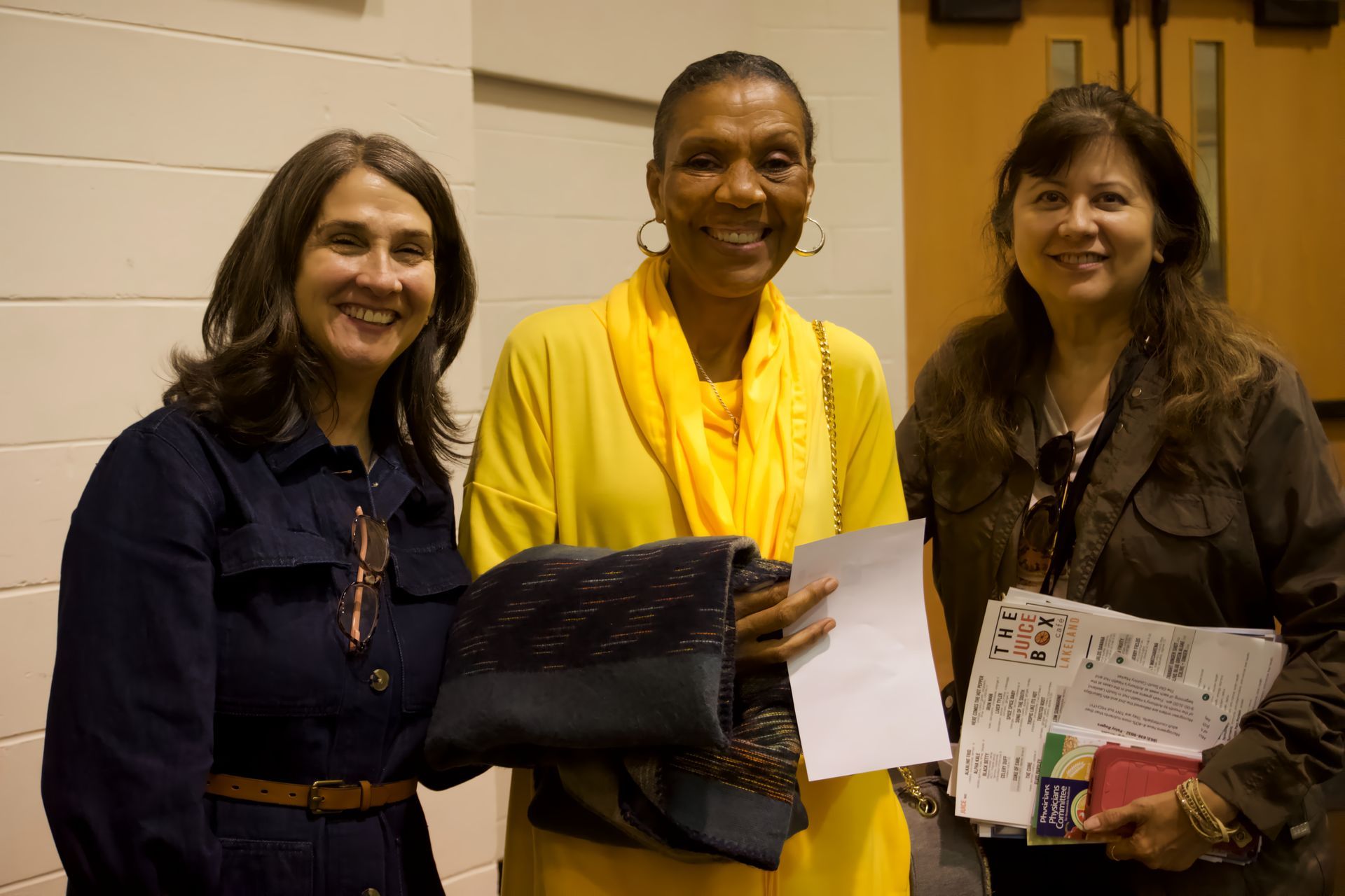 Three women are posing for a picture and one of them is wearing a yellow scarf