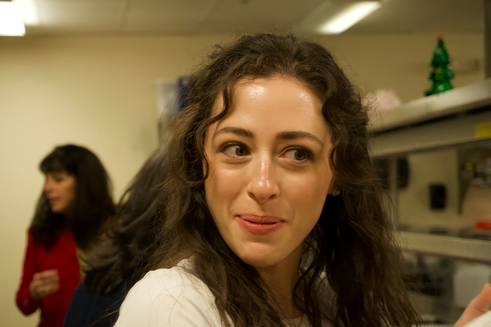 A woman is making a funny face in a kitchen with a christmas tree in the background.