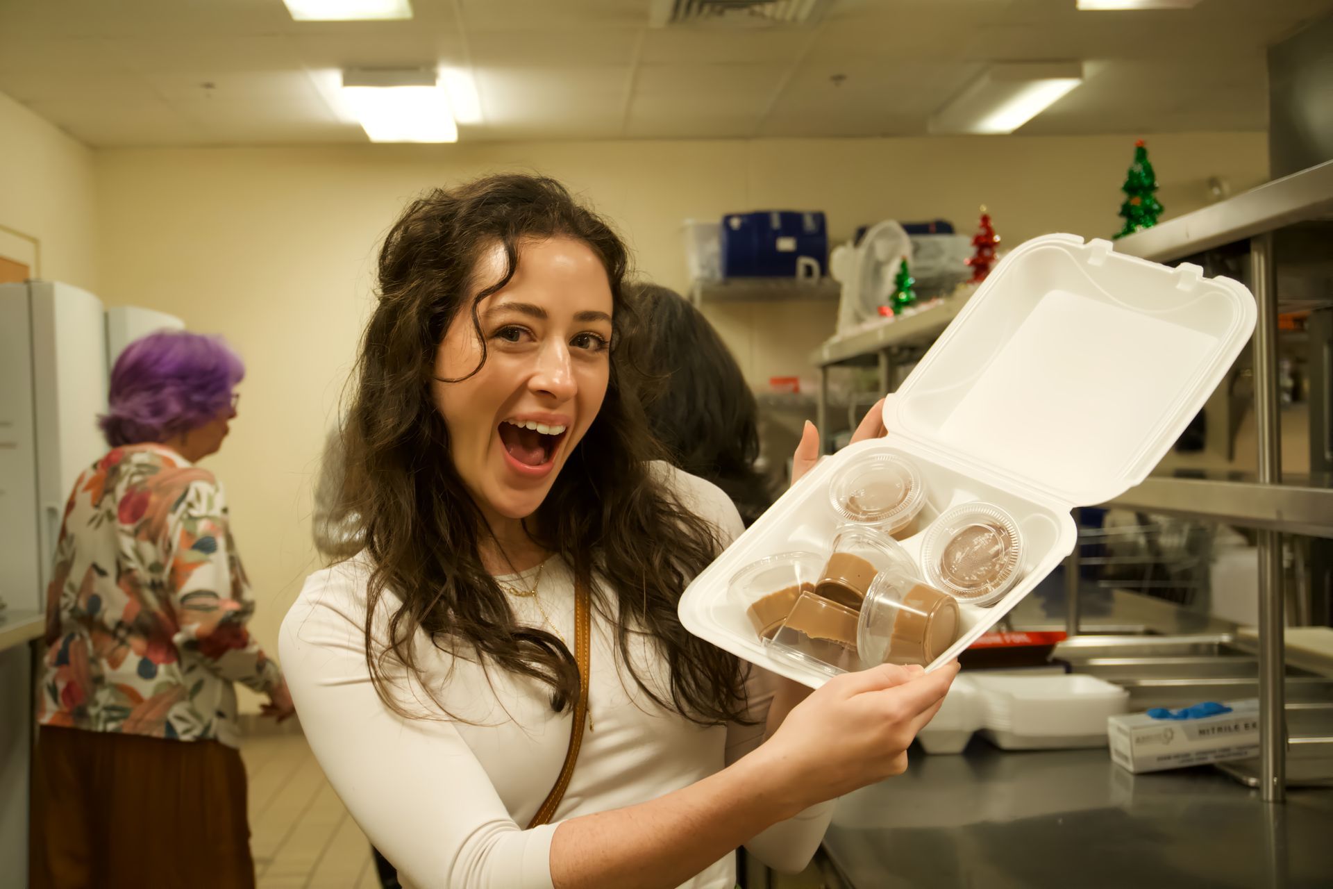 A woman is holding a styrofoam container of food in a kitchen.