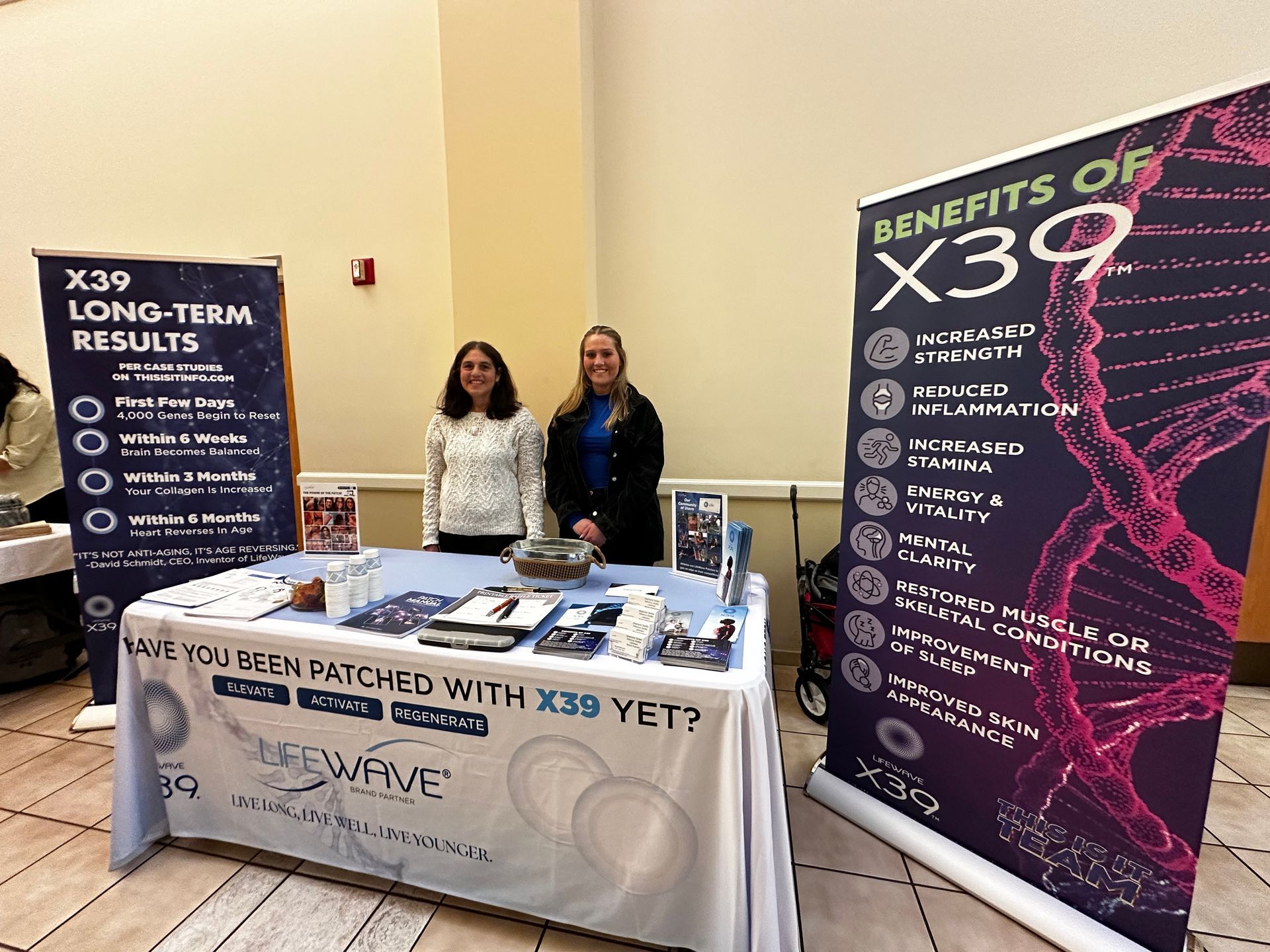 Two women are standing in front of a table with a sign that says `` benefits of x39 ''.