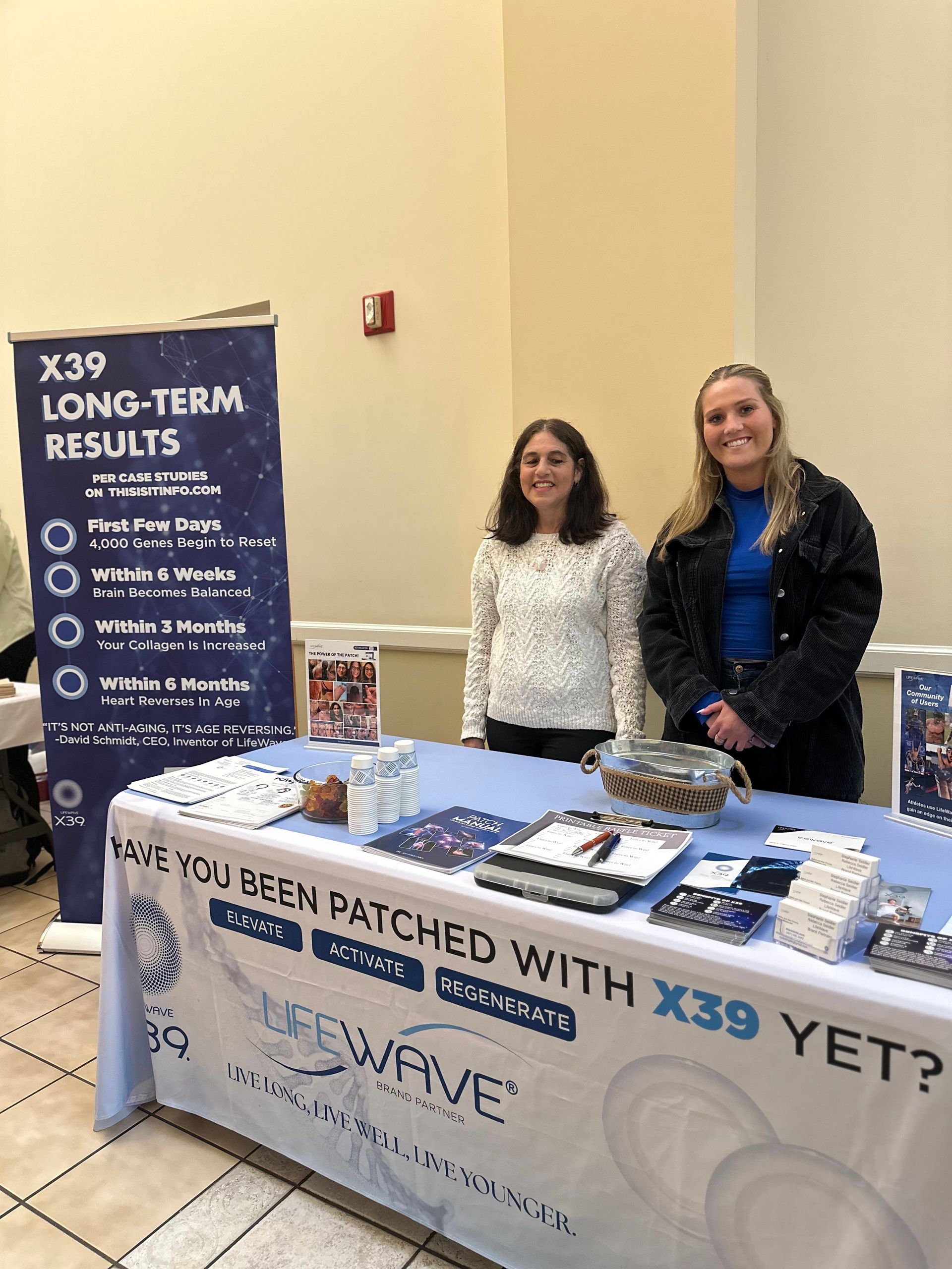 Two women are standing behind a table with a sign that says `` have you been patched with x39 yet ? ''