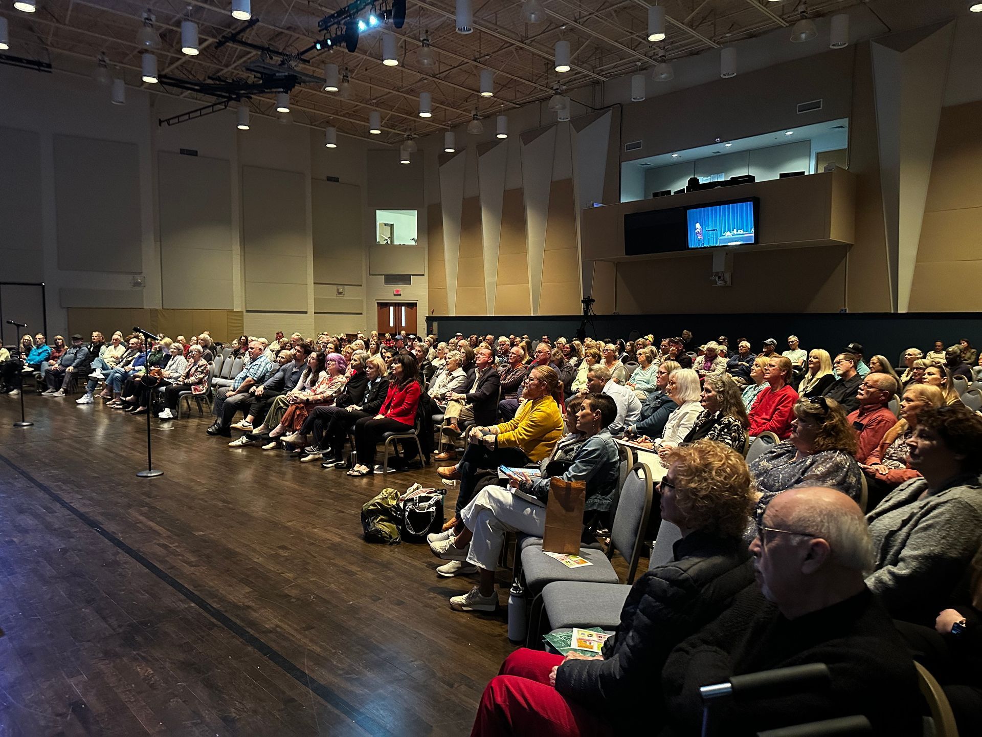 A large group of people are sitting in a large auditorium watching a presentation.