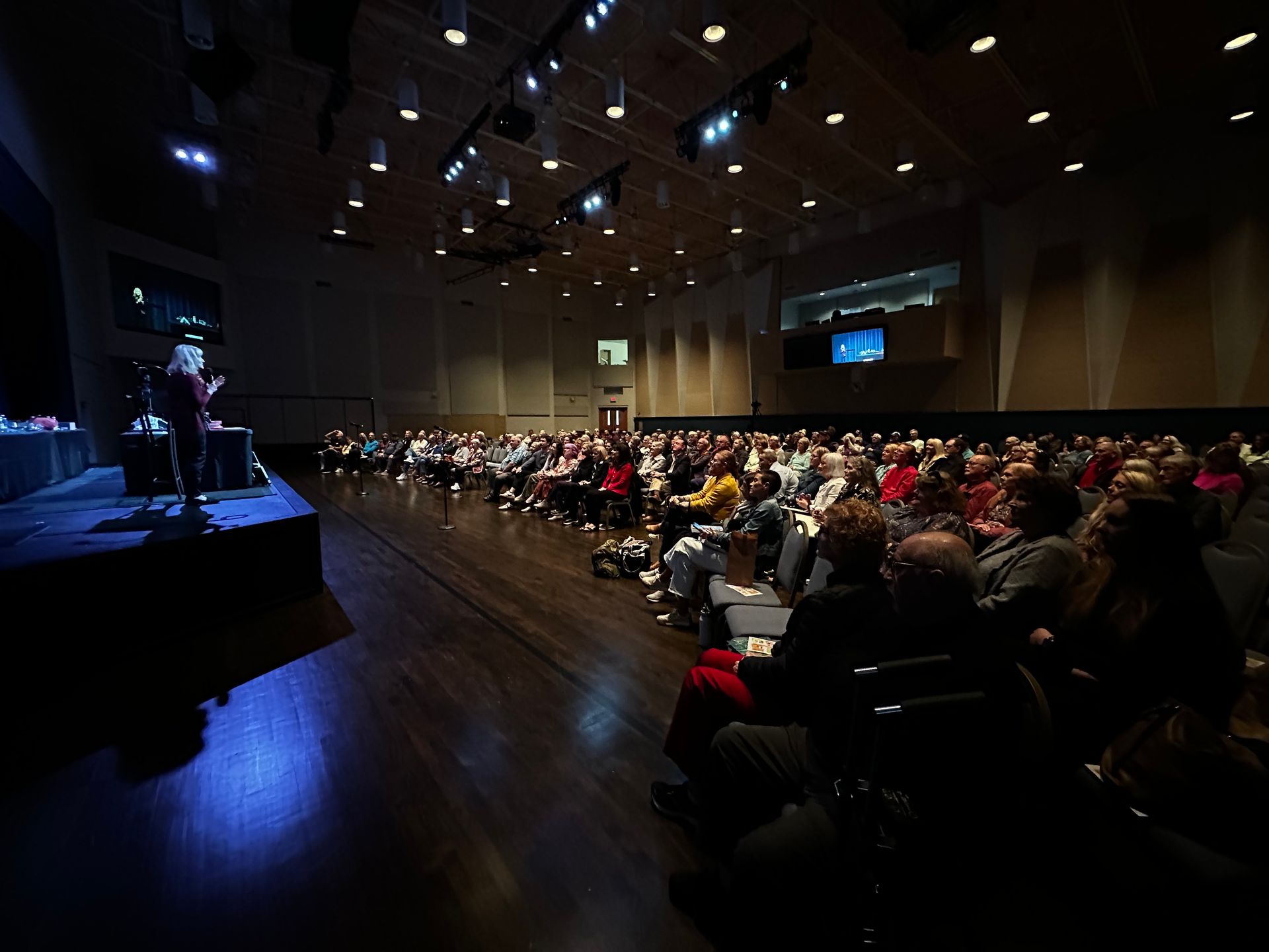 A woman is giving a presentation in front of a crowd in a large auditorium.