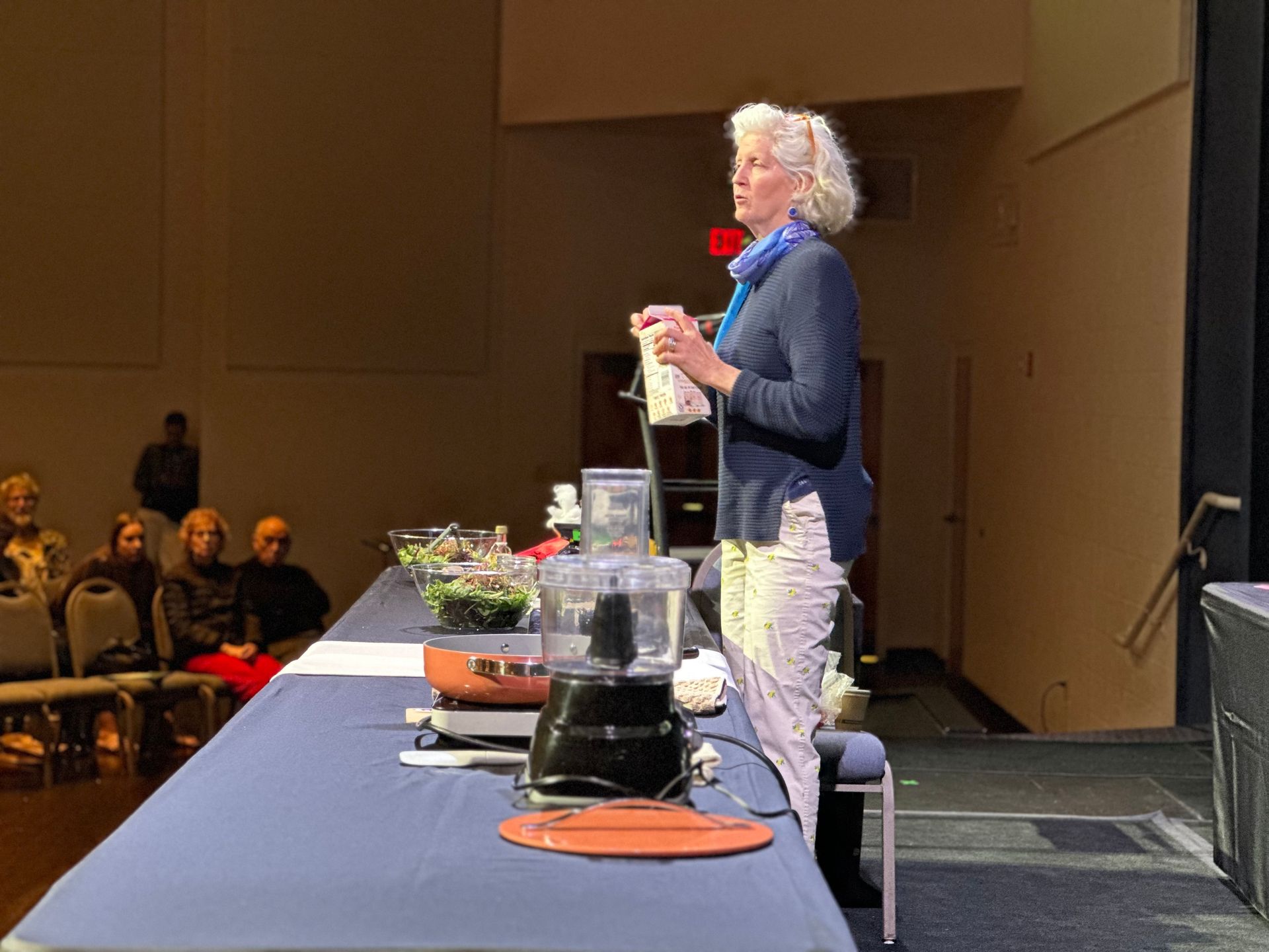 A woman is standing in front of a table with a blender on it.