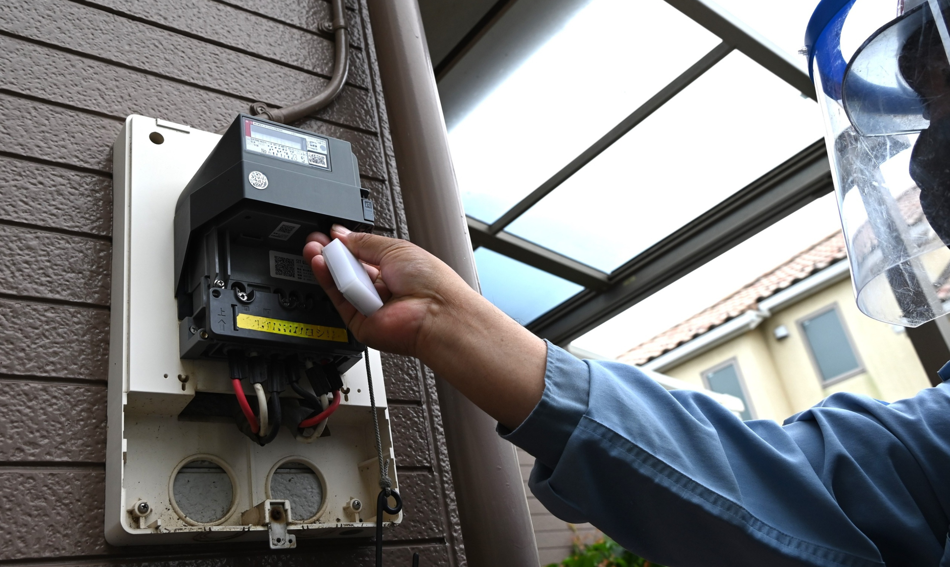 Person interacting with an electrical meter on a building's exterior. They are holding a white device. Person interacting with an electrical meter on a building's exterior. They are holding a white device.
