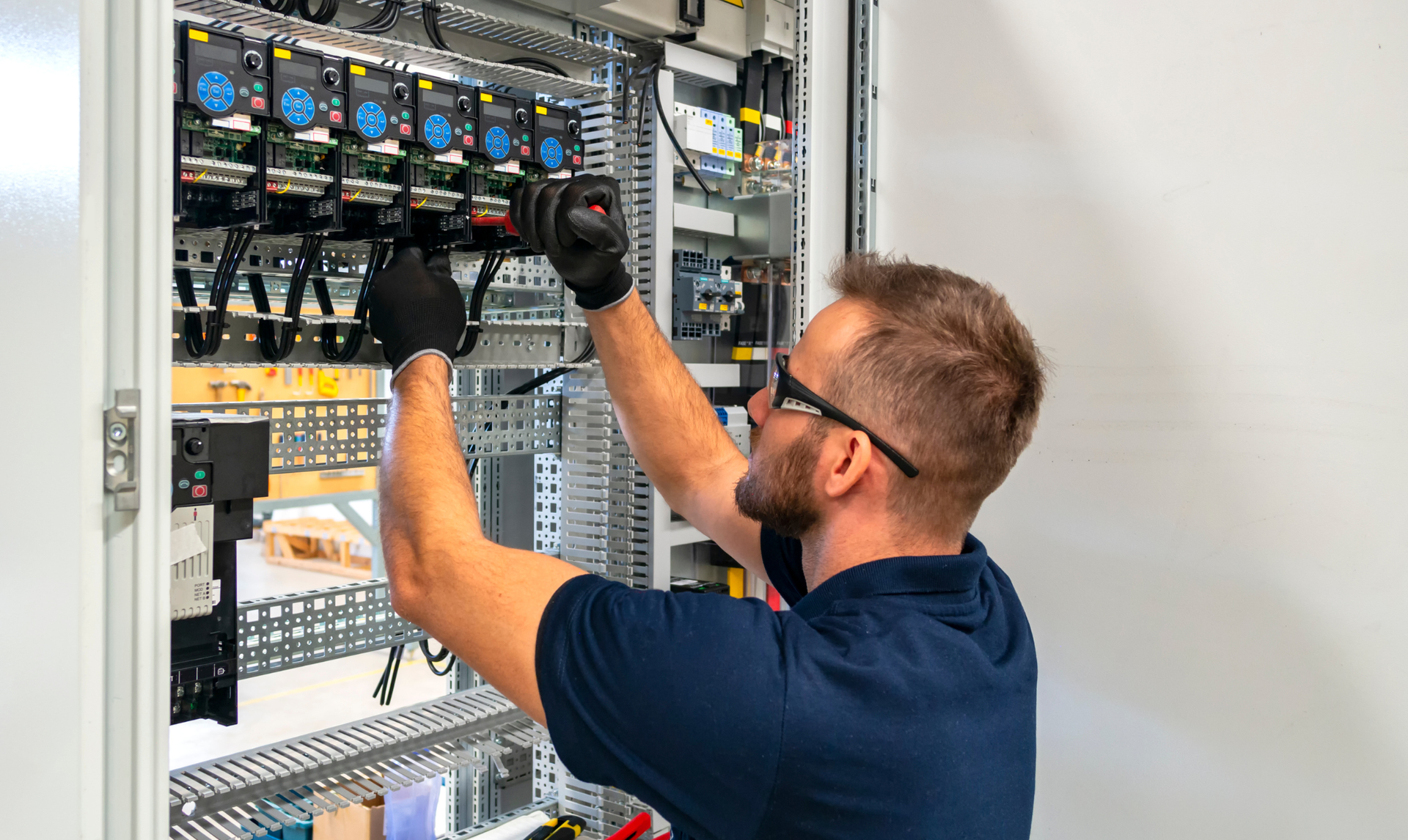 Man in safety glasses and gloves working on electrical panel.
