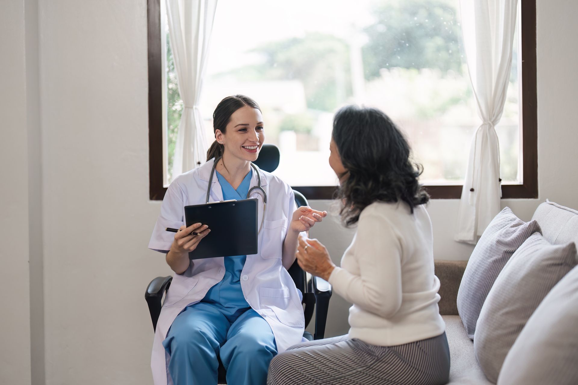 A nurse is sitting on a bed talking to a patient.