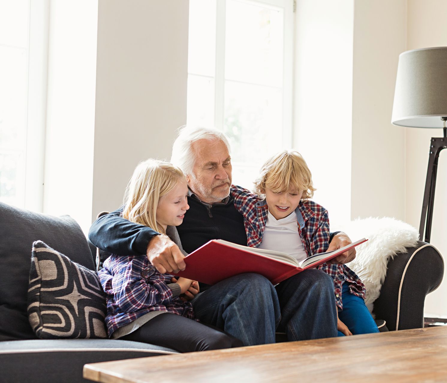 A man and two children are sitting on a couch reading a book.
