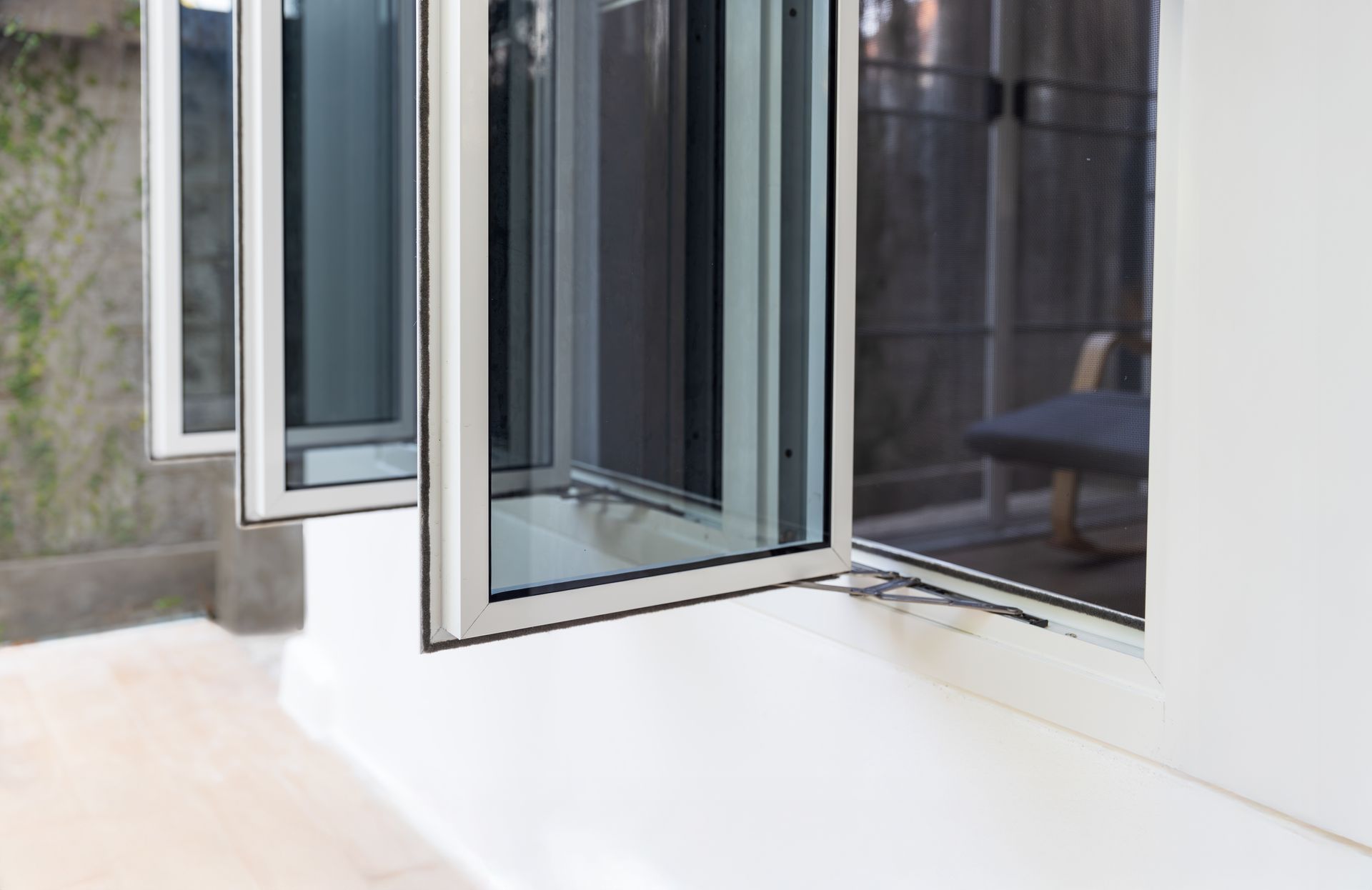 Open glass door leading to a white patio beside a gray building wall.