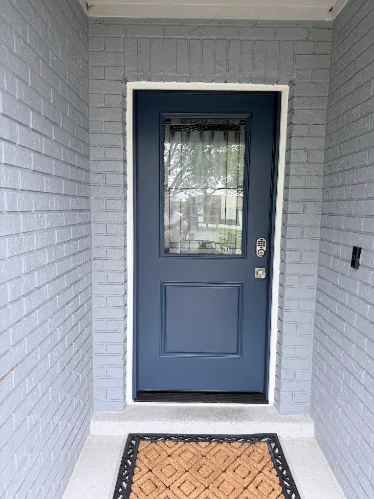 Blue front door with window and welcome mat in a gray brick entryway