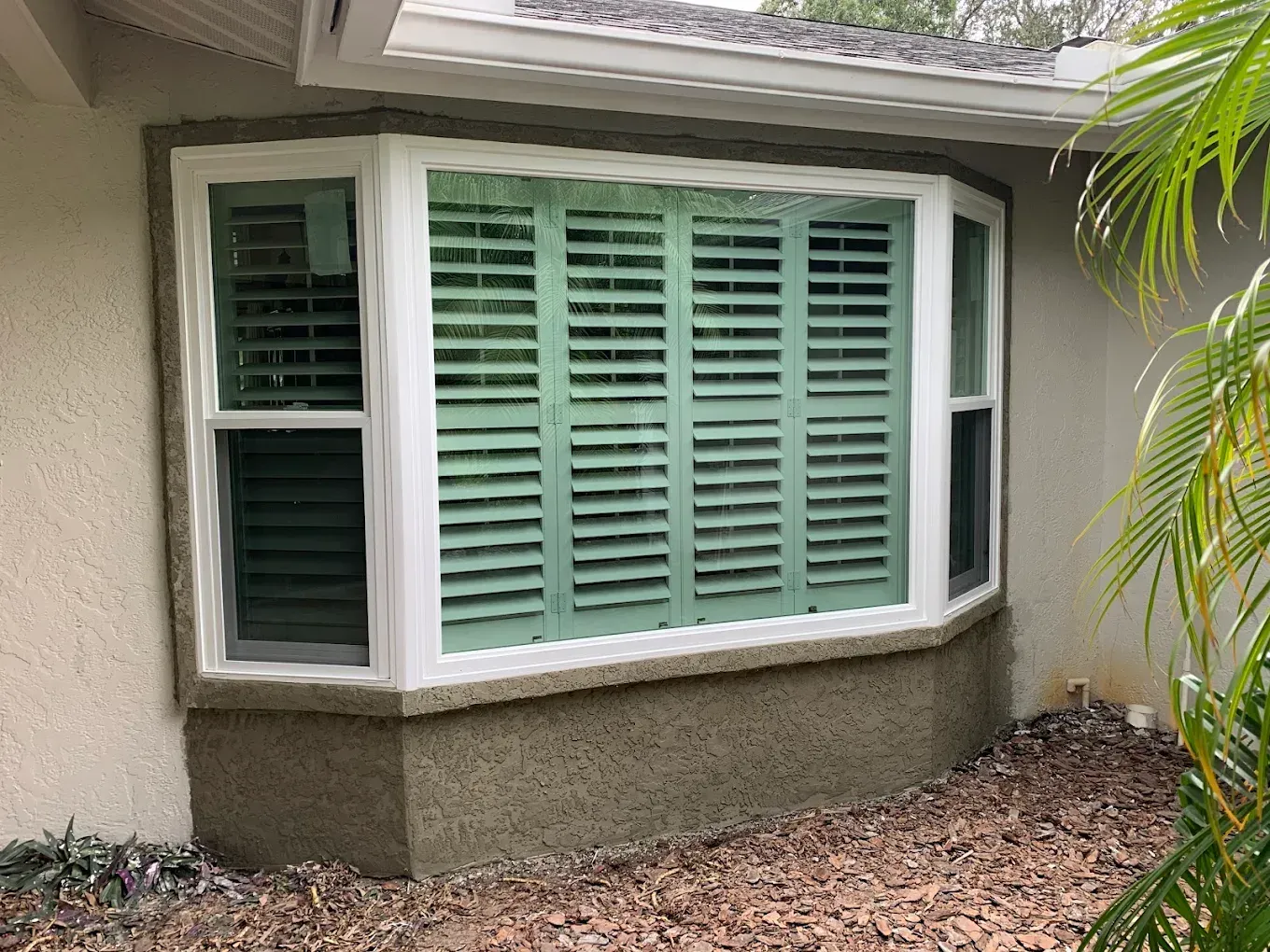 House exterior with a bay window and pale green shutters beneath a roof overhang.