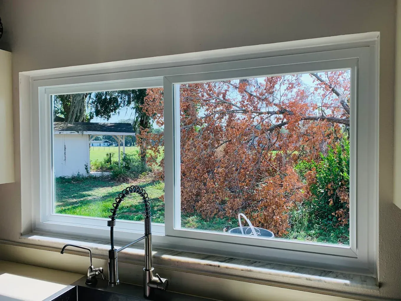 Kitchen sink beneath a window with a view of a green yard and red-leaved tree