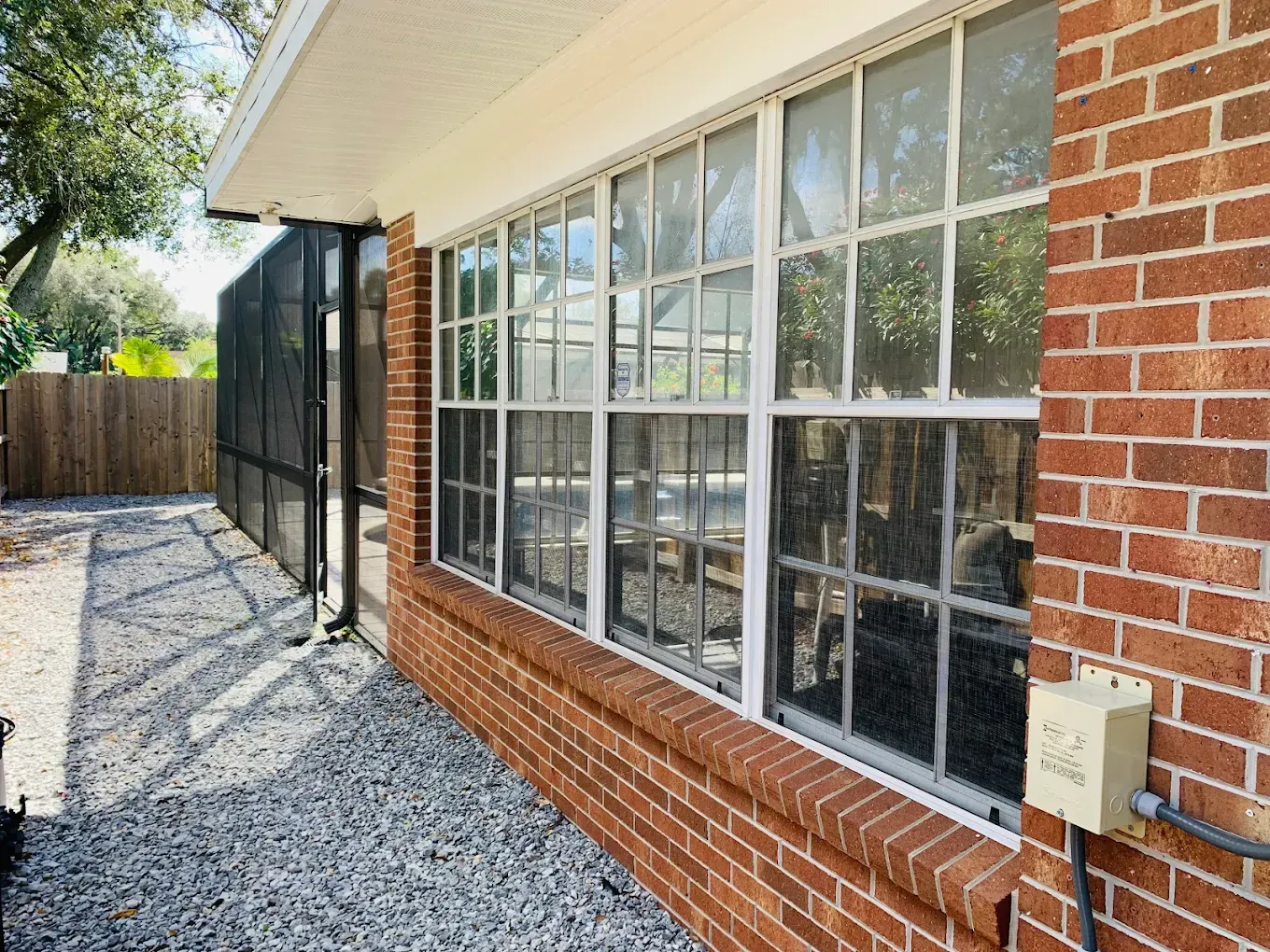 Brick house side yard with large windows, gravel path, and a screened porch under a bright sky