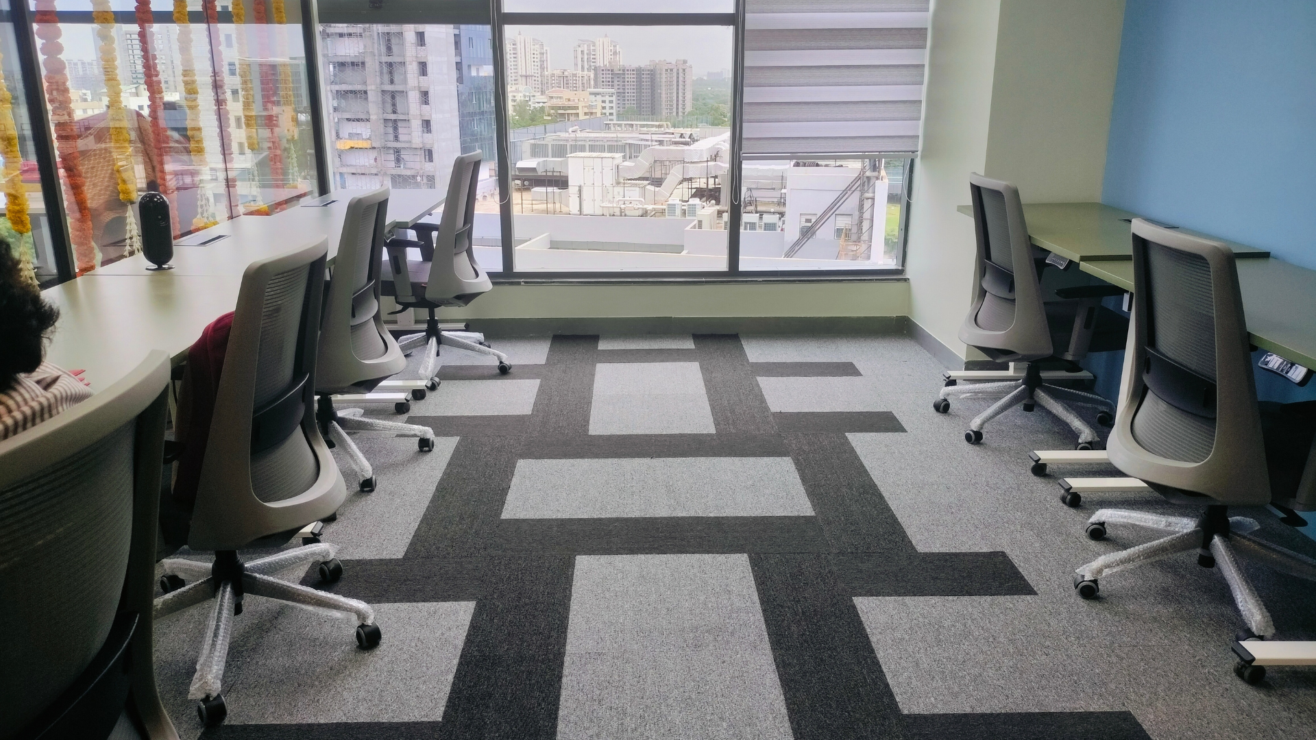 A bright office space with rows of empty desks, ergonomic chairs, and a patterned carpet facing a large window view.