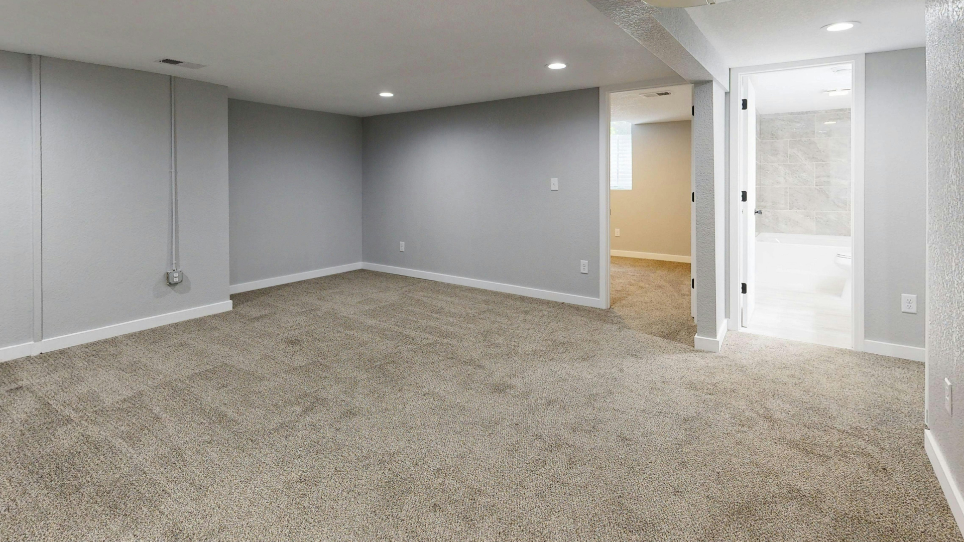 An empty, finished basement with gray walls, neutral patterned carpet, recessed lighting, and an open doorway.