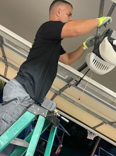 A man is standing on a ladder working on a garage door opener.