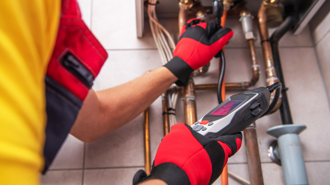 Gloved hands using a wrench to tighten plumbing pipes under a sink