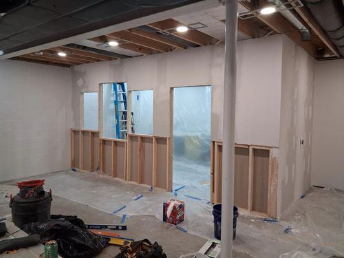 Renovation in progress in a room with exposed studs, plastic sheeting, ladder, and unfinished walls.