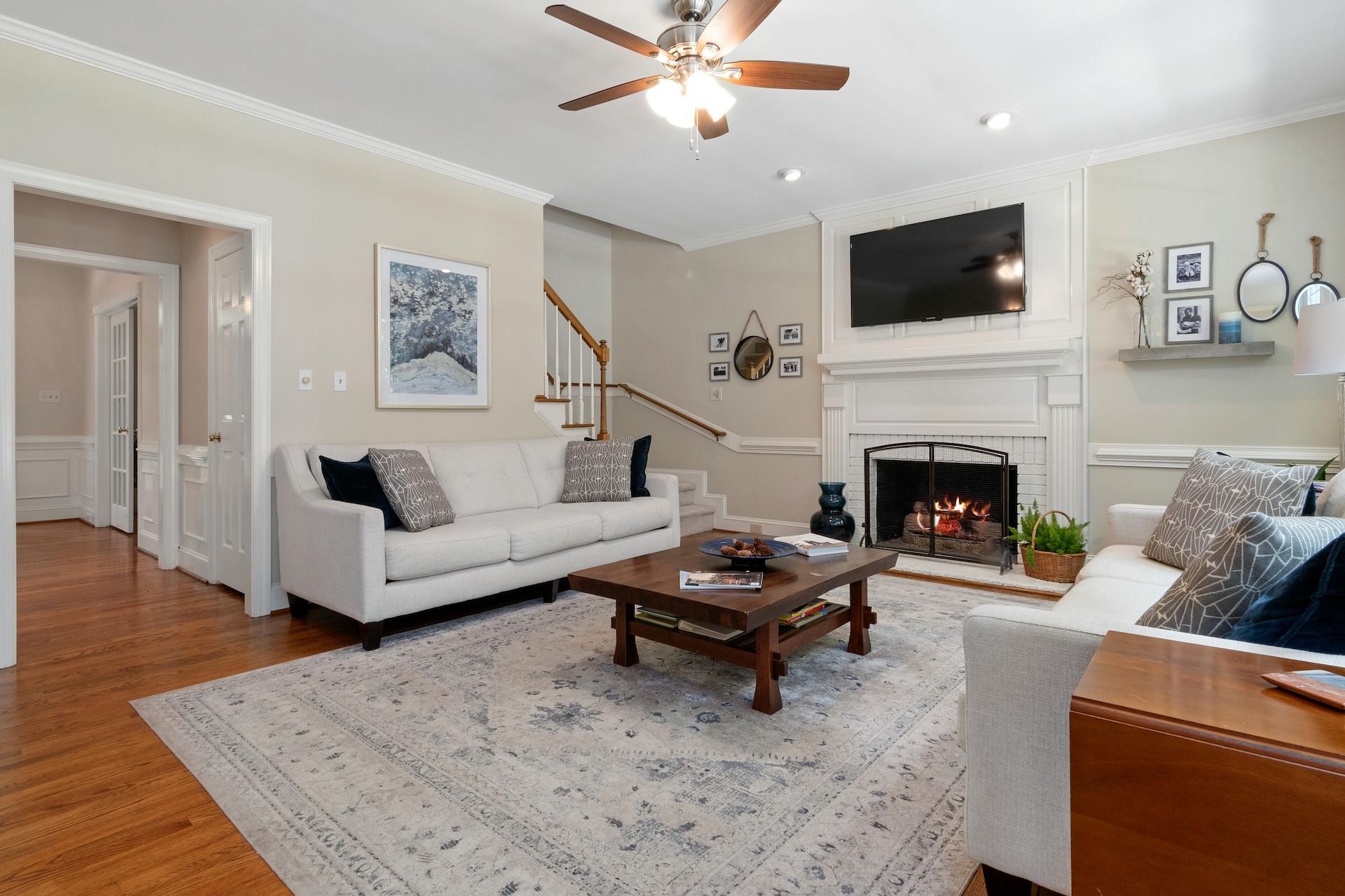 Bright living room with white sofas, fireplace, wall-mounted TV, and wooden coffee table
