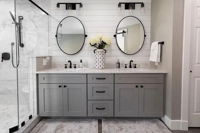 Modern double-sink bathroom vanity with gray cabinets, two round mirrors, wall sconces, and a vase of flowers.