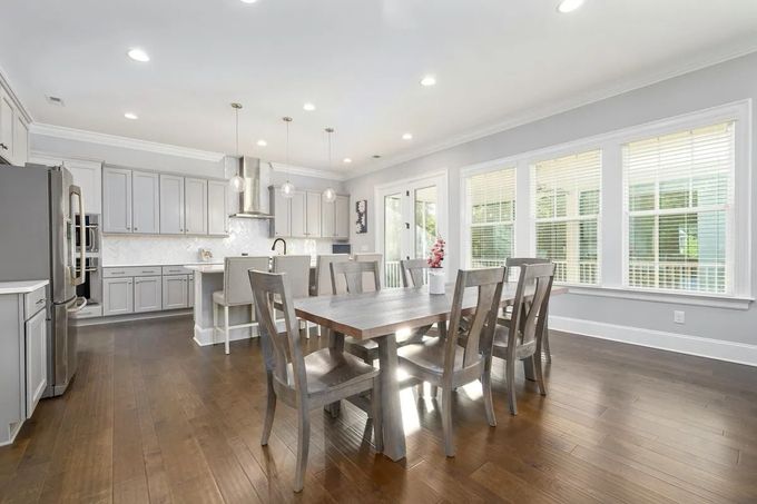 Bright modern kitchen and dining area with white cabinets, wood floors, and a dining table by large windows