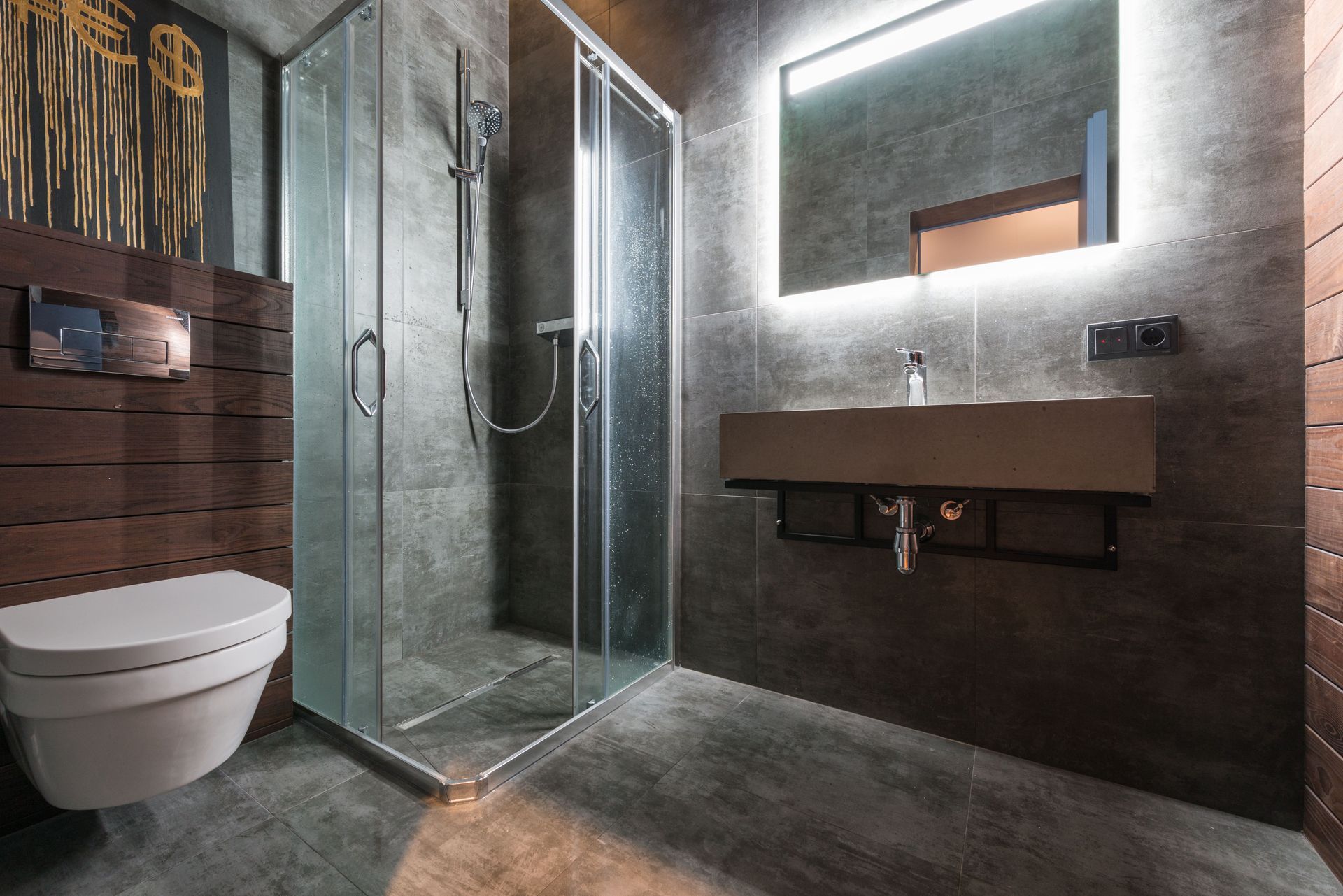 Modern gray bathroom with glass shower, wall-mounted sink, and toilet