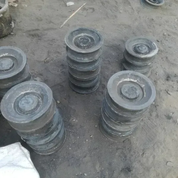 Varias poleas de metal gris apiladas sobre una superficie arenosa.