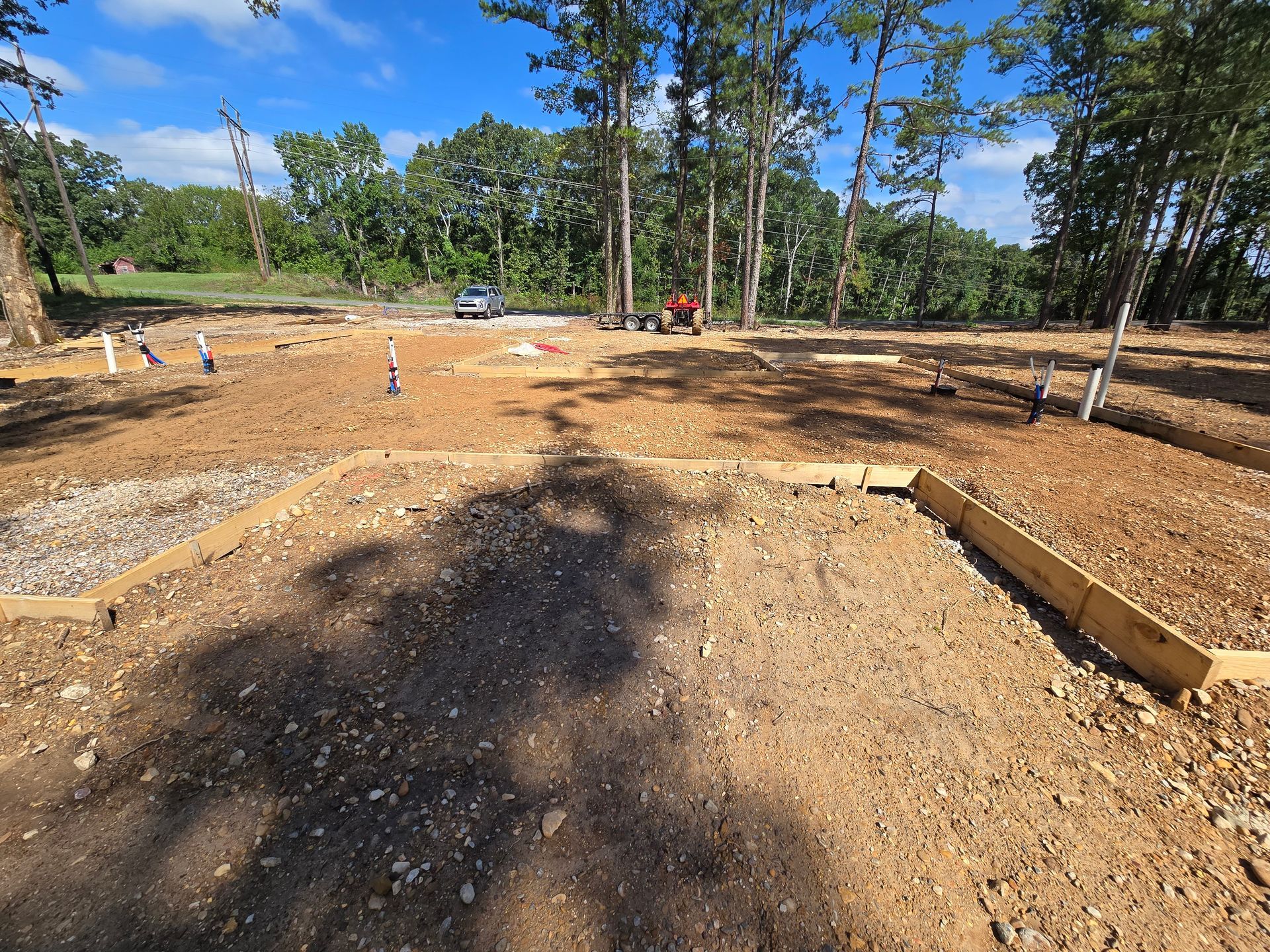 Dirt plots framed by wood, construction site, trees in the background.