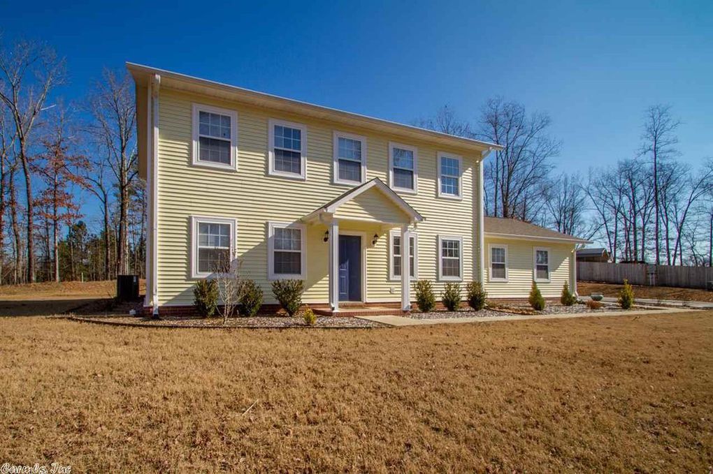Yellow two-story house with blue door and windows. Bare trees and brown yard under a blue sky.