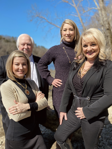 Four people pose outdoors near water: two women in front, two in back, smiling.