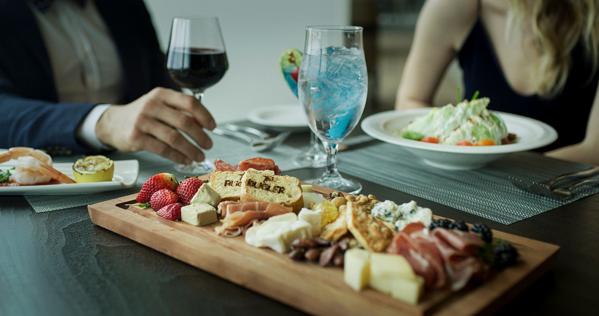 Couple dining at a restaurant, sharing a charcuterie board, wine, and salad.