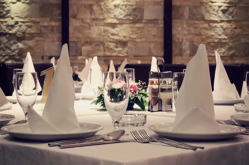 A formal dining table set with white linen, folded napkins, and glassware in a restaurant.