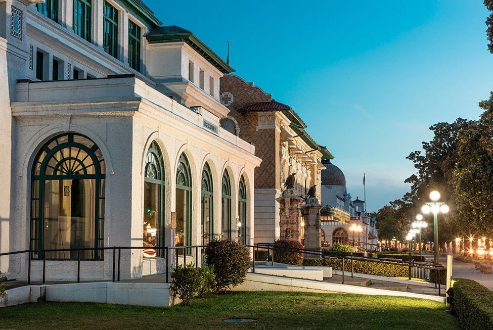 Historic building at dusk with arches, columns, and decorative statues along a tree-lined street.