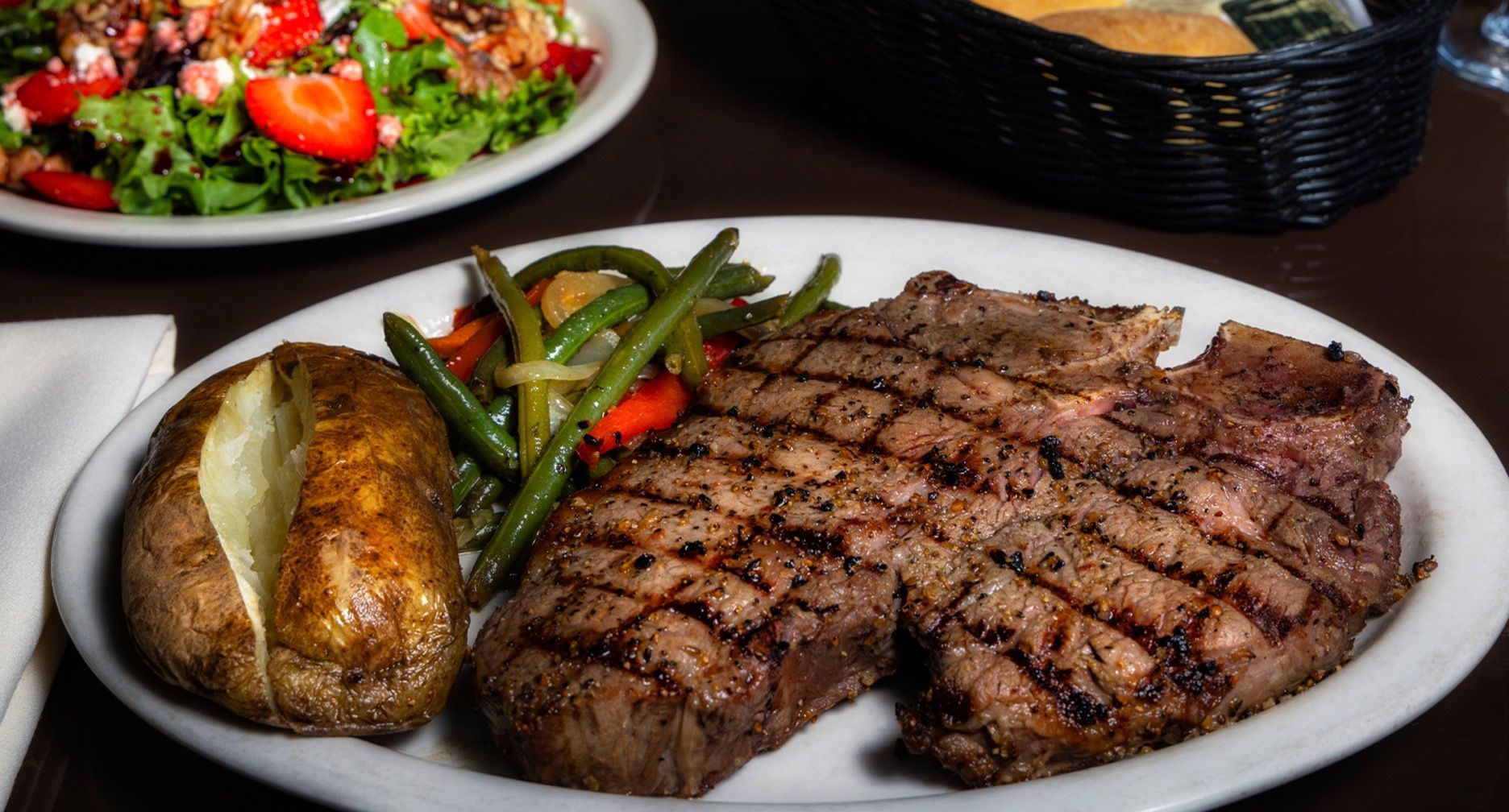 Grilled steak with baked potato, green beans, and salad on a table.